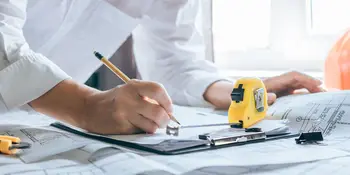 Person am Reißbrett mit Stift, Plan und Massband (Symbolbild)